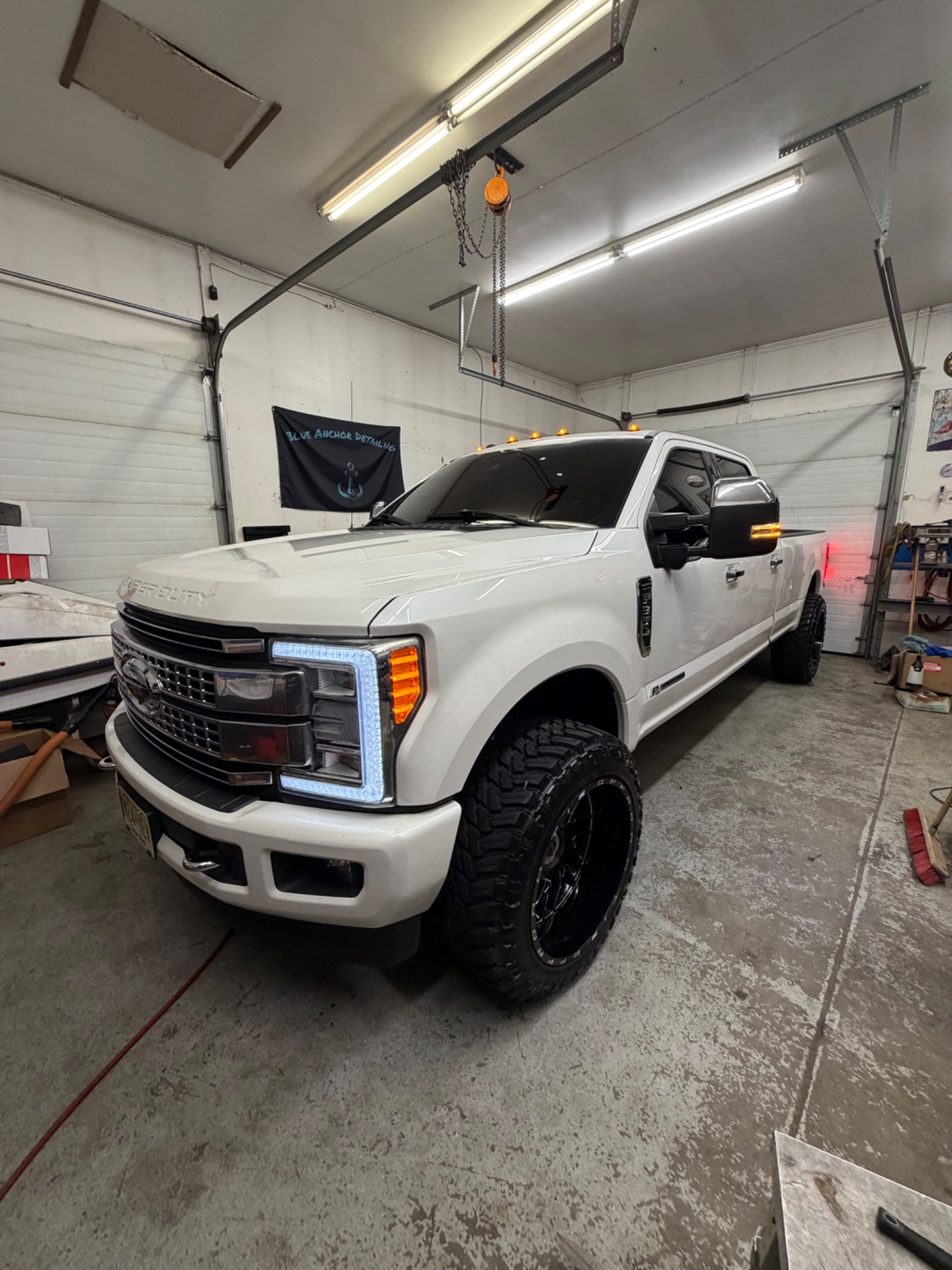 Lifted white Ford F-350 Super Duty on black wheels inside the Blue Anchor detailing bay