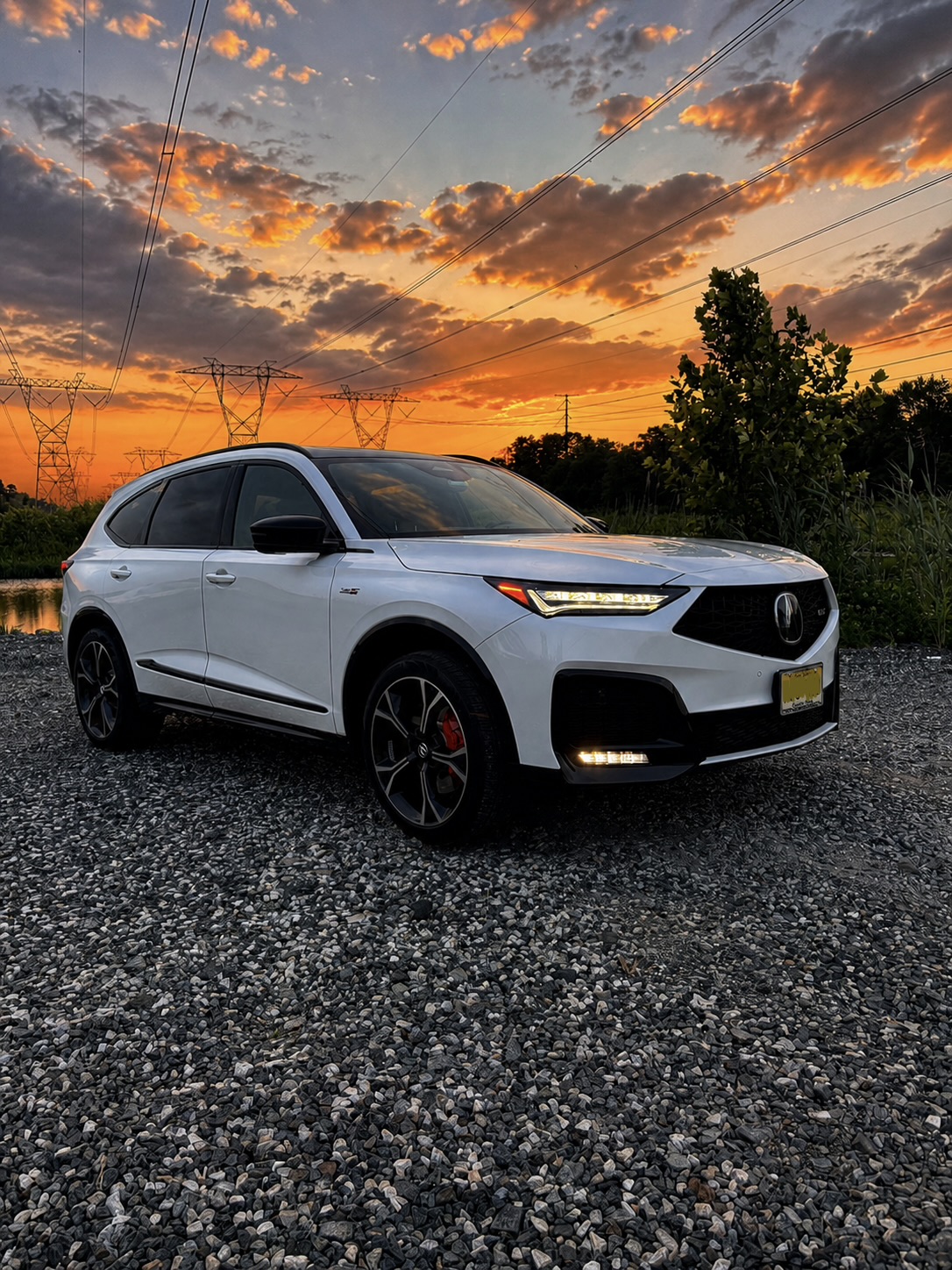 White Acura MDX Type S parked on gravel under an orange sunset sky