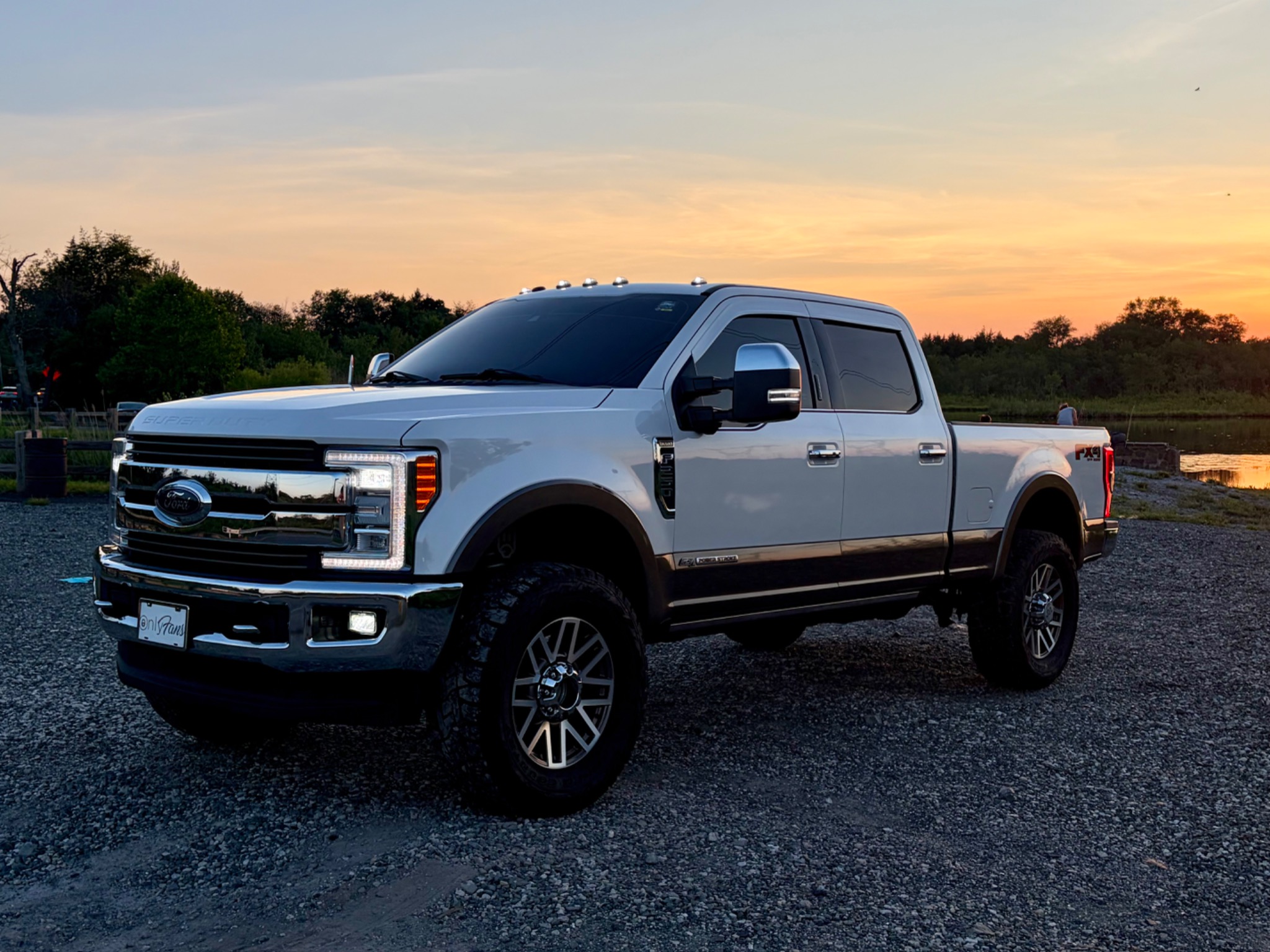 White Ford F-350 Super Duty King Ranch with a high-gloss finish parked on gravel at sunset